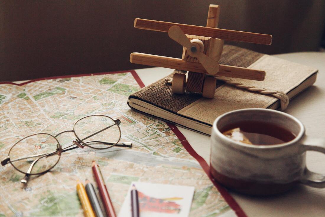 Model airplane alongside a map, a journal, a cup of coffee, and some eyeglasses
