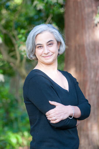 Author photo of Laurie Frankel with gray hair in a black shirt in front of a tree trunk